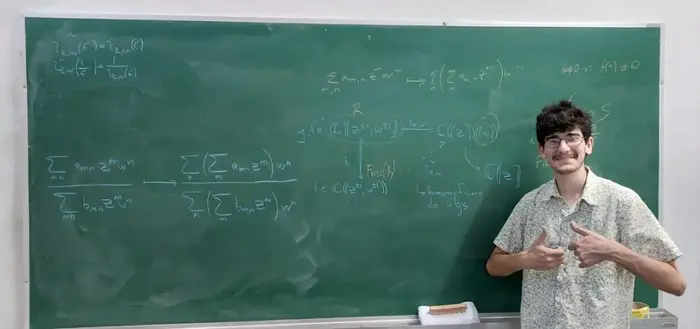 A picture of Thiago in front of a green blackboard containing some formulas concerning formal power series and a commutative diagram.